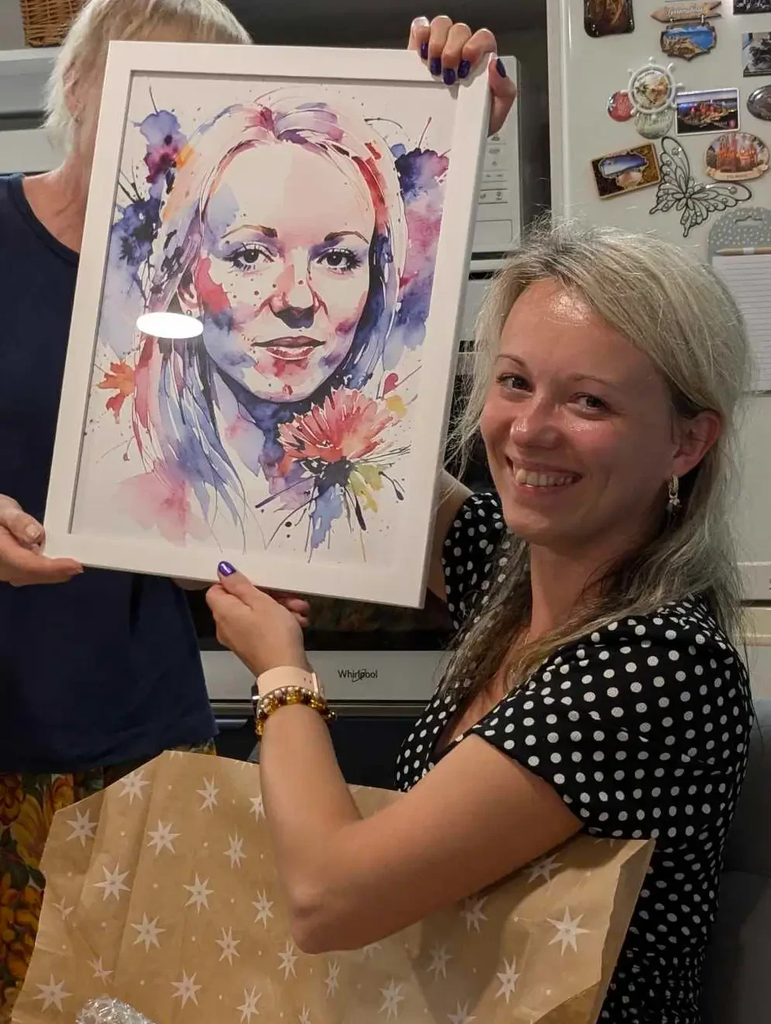 Personalized Artwork. Woman smiling while holding a framed watercolor portrait with blue, pink, and red paint splashes